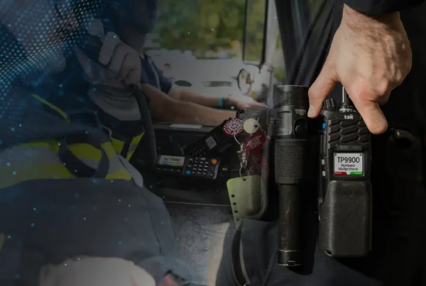 Tait 9900 mobile radio and a first responder holding it while it is on their belt